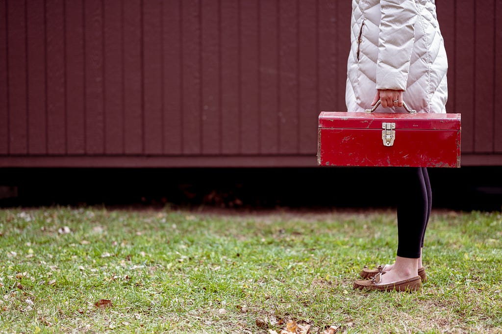 A close up photo of a woman holding a red toolbox.