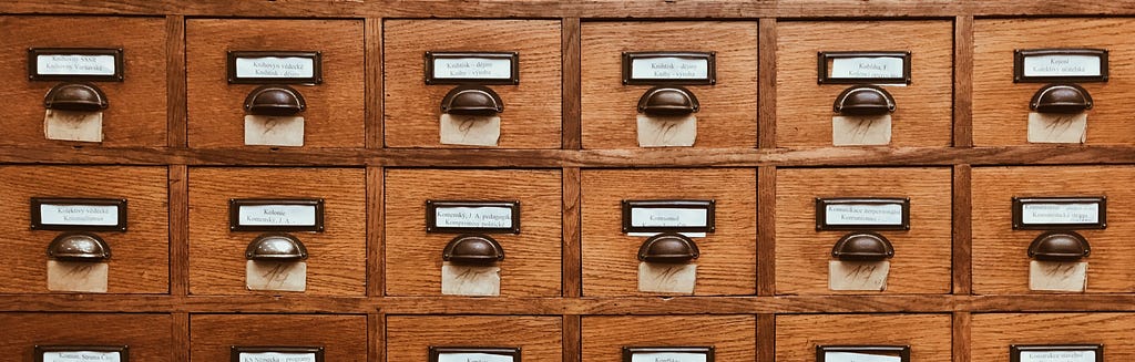 Picture of an apothecary's old wooden drawers with metal half moon pulls and white paper labels on the front