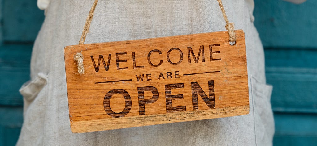 wood sign with written text on it: welcome — we are open.