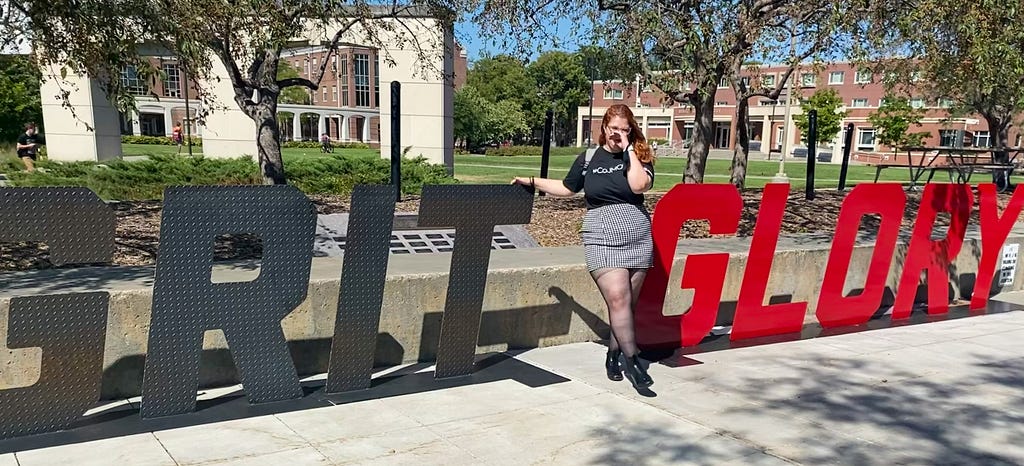 Maggie poses for a photo with signs that read “Grit” and “Glory”