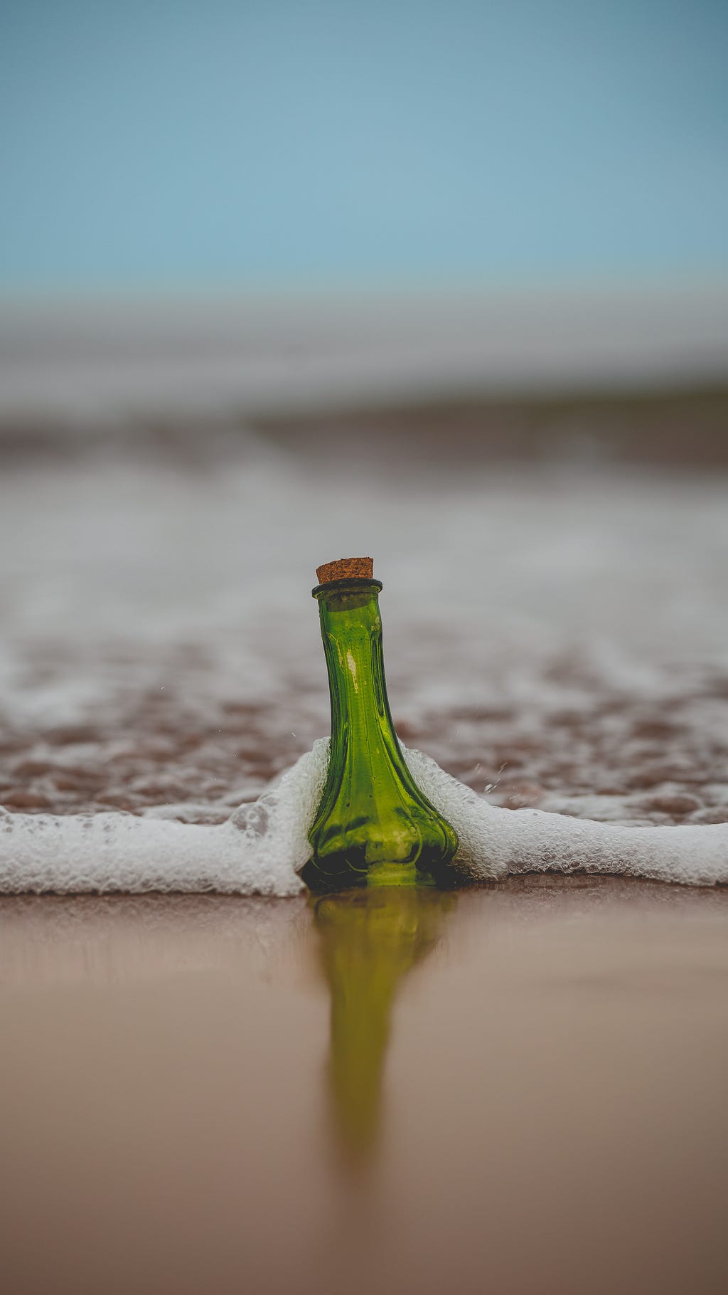 A green bottle surrounded by sea foam on a beach