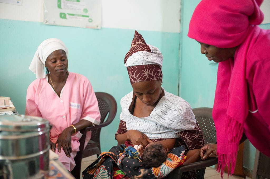 A new mother breast feeds her infant as two health workers observe.