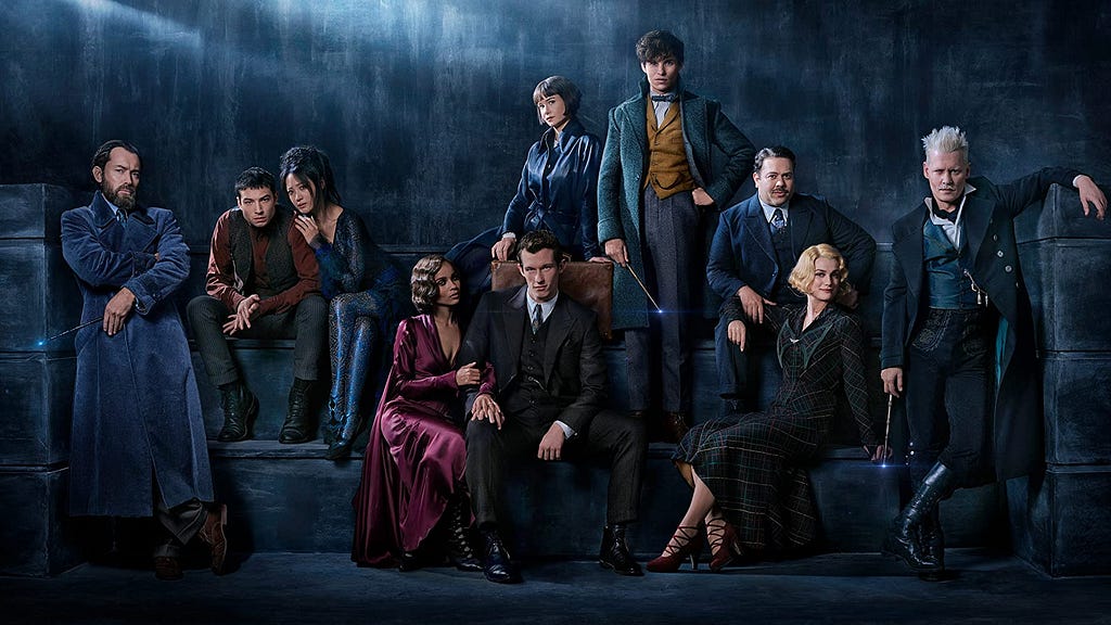 The cast of Fantastic Beasts 2 dressed as their characters in front of a blue dark background.