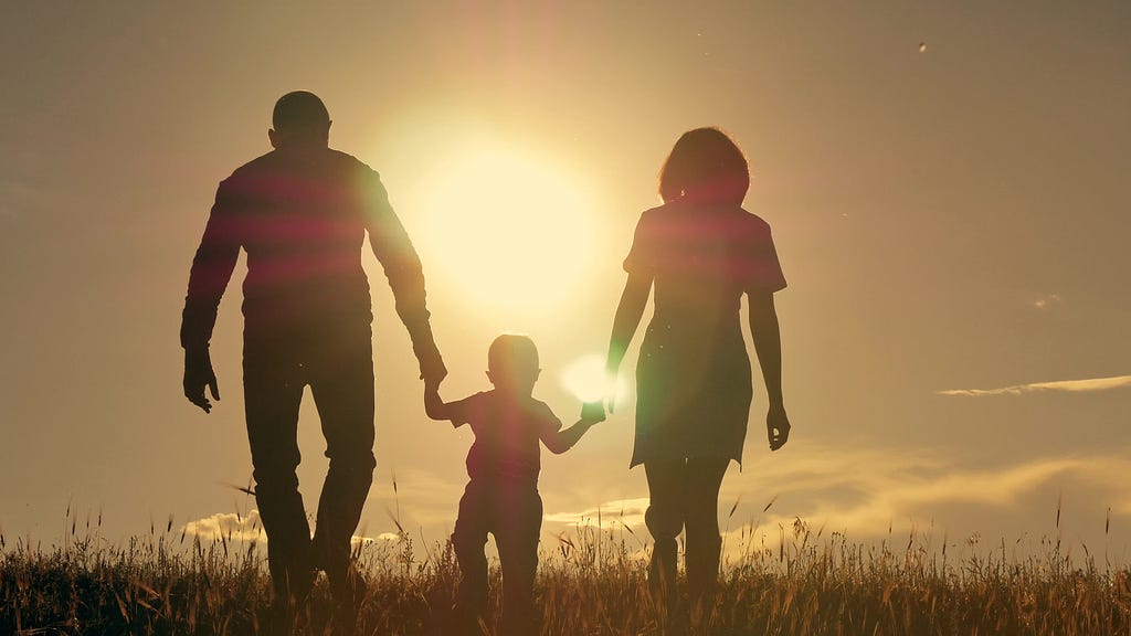 Families and children can be agents of change for a more peaceful world. Silhouette of parents holding hands with their young child as they walk through a field toward a bright sunset. (Photo/ by Alexey Logvinenko, pond5.com)