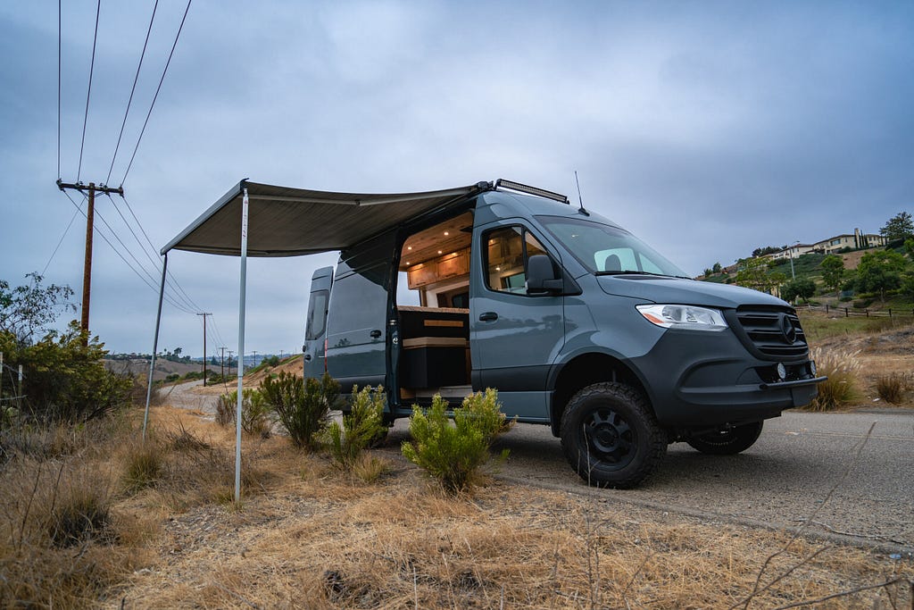 Mercedes Sprinter camper in grey with side door open, internal lights on, and awning out