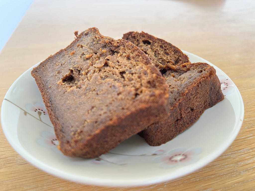 Photograph of two slices of banana bread on a small china plate, placed on a wooden surface.