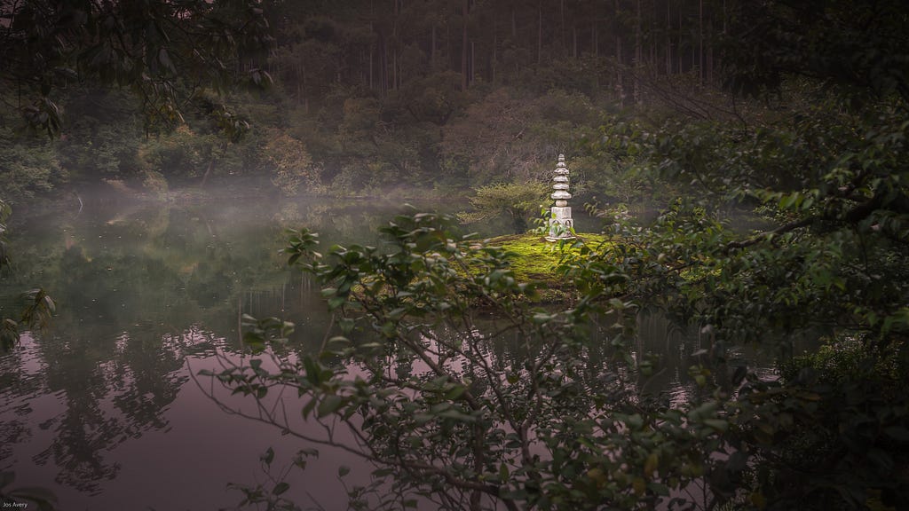A stone monument called the White Snake Pagoda at the Golden Pavilion sits on a green islet in the middle of a small pond.