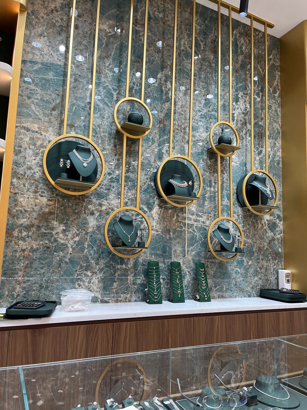 A display of diamond and gold necklaces, ear tops, pendants and chains on a green and light orange granite slab.