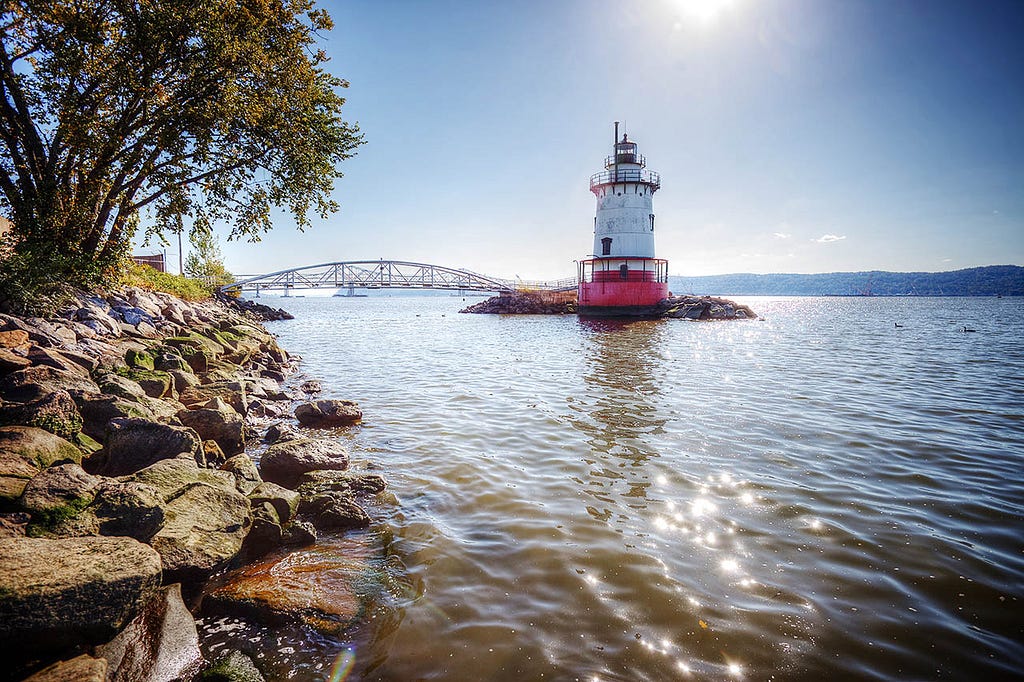 A lone red and white lighthouse guards a vast expanse of blue water.