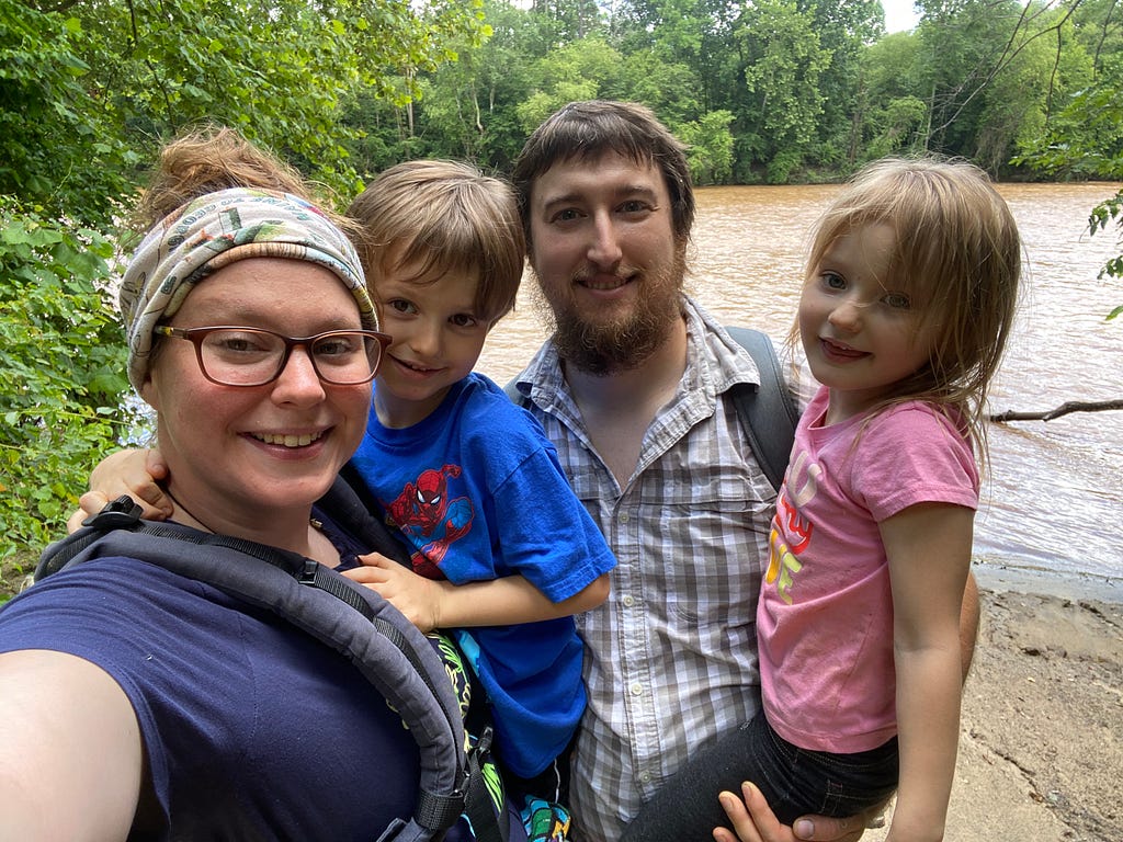 A family of four poses for a photo with a river in the background.