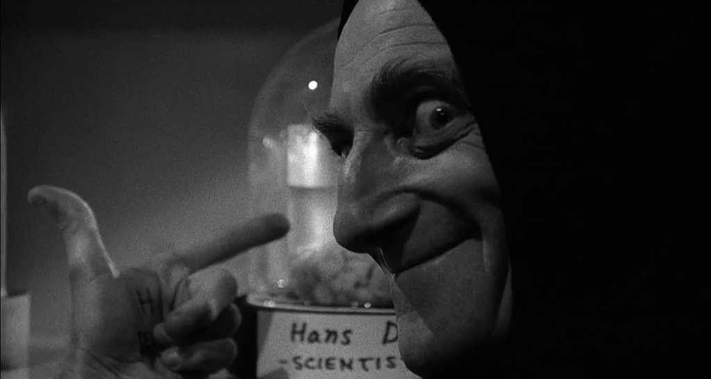 A still from the Mel Brooks comedy “Young Frankenstein” (1974) showing Marty Feldman (as Igor) visiting the “brain depository” to collect a brain for his master. He is pointing to a brain in a jar (labelled “scientist”) and smiling to the camera.