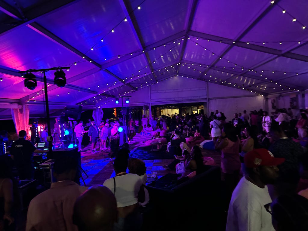 Dark purple LED lighting glowing off the top of a tent while a large audience listens to an R&B band.