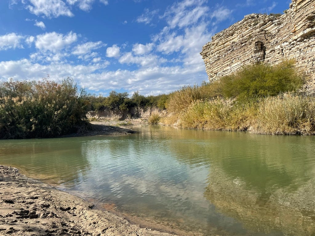 A view of the Rio Grande with a limestone cliff behind it.