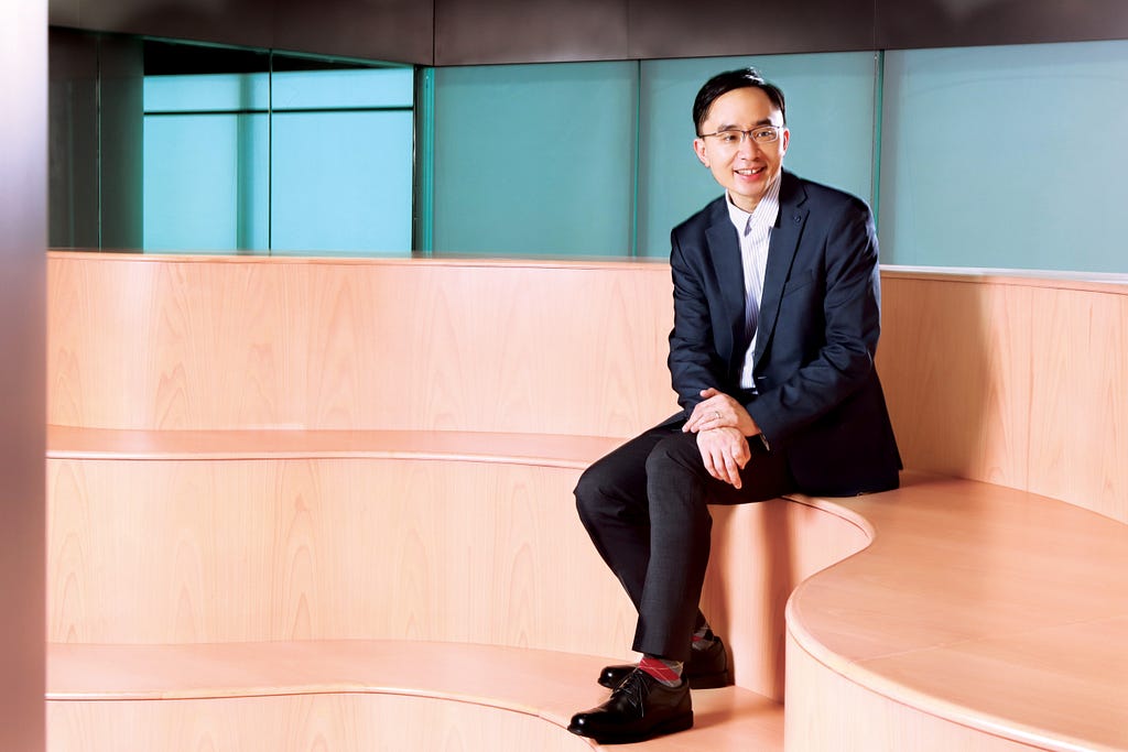 Dr Victor Lee Ho-fun from HKUMed sitting on the indoor steps in a formal suit.