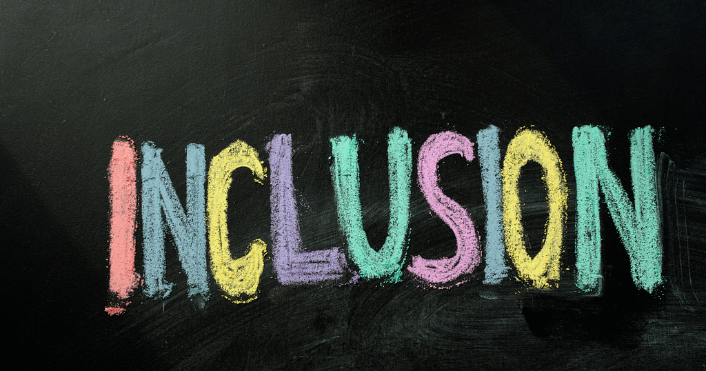 The word “Inclusion” is handwritten on a blackboard with colored letters.