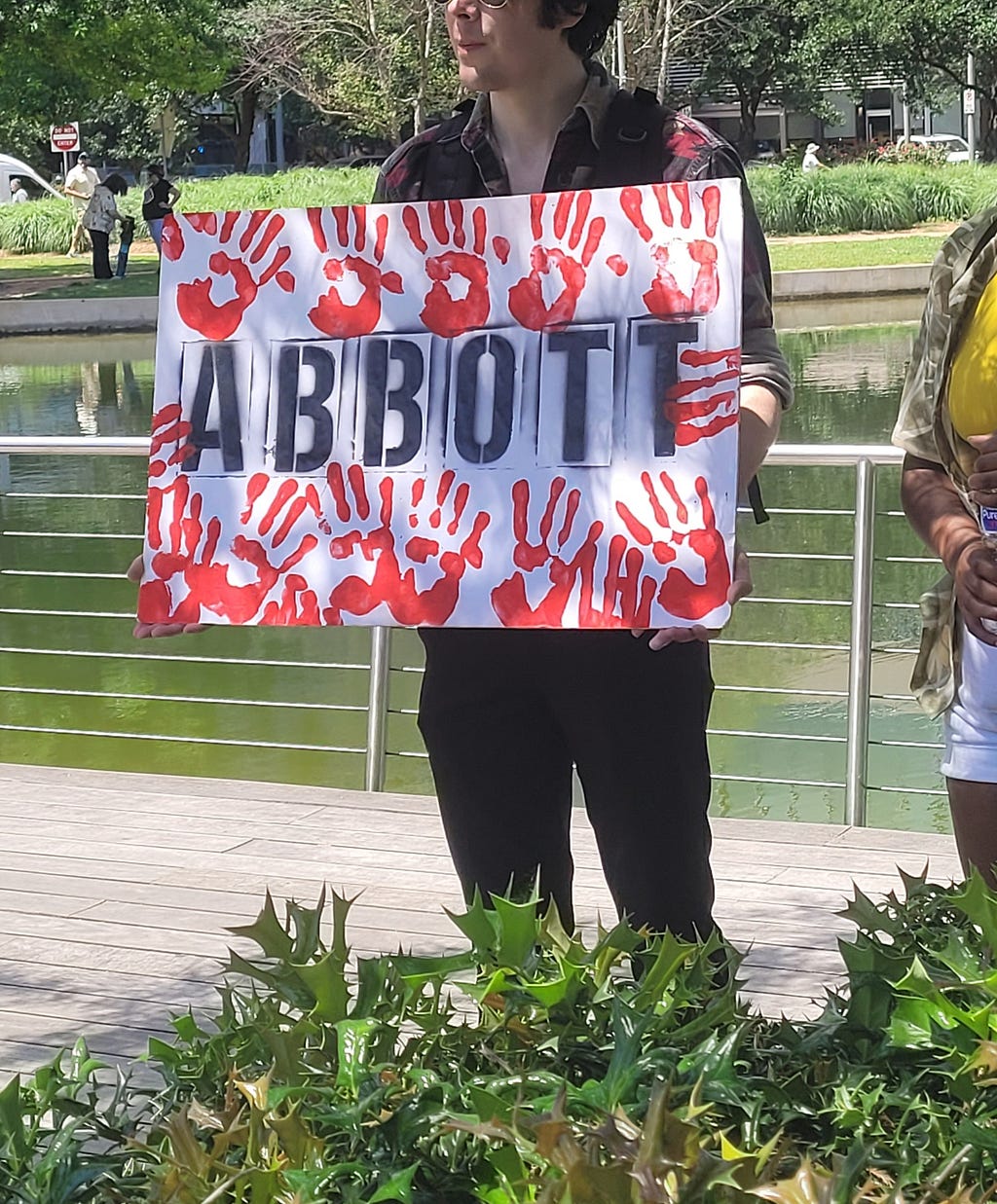 An anti gun violence protester raises a sign showing red hand prints around the name “Abbott,” referring to Governor Greg Abbott.