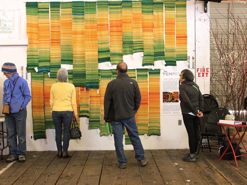 A collection of knitted Tempestries hanging vertically on the wall of a gallery.