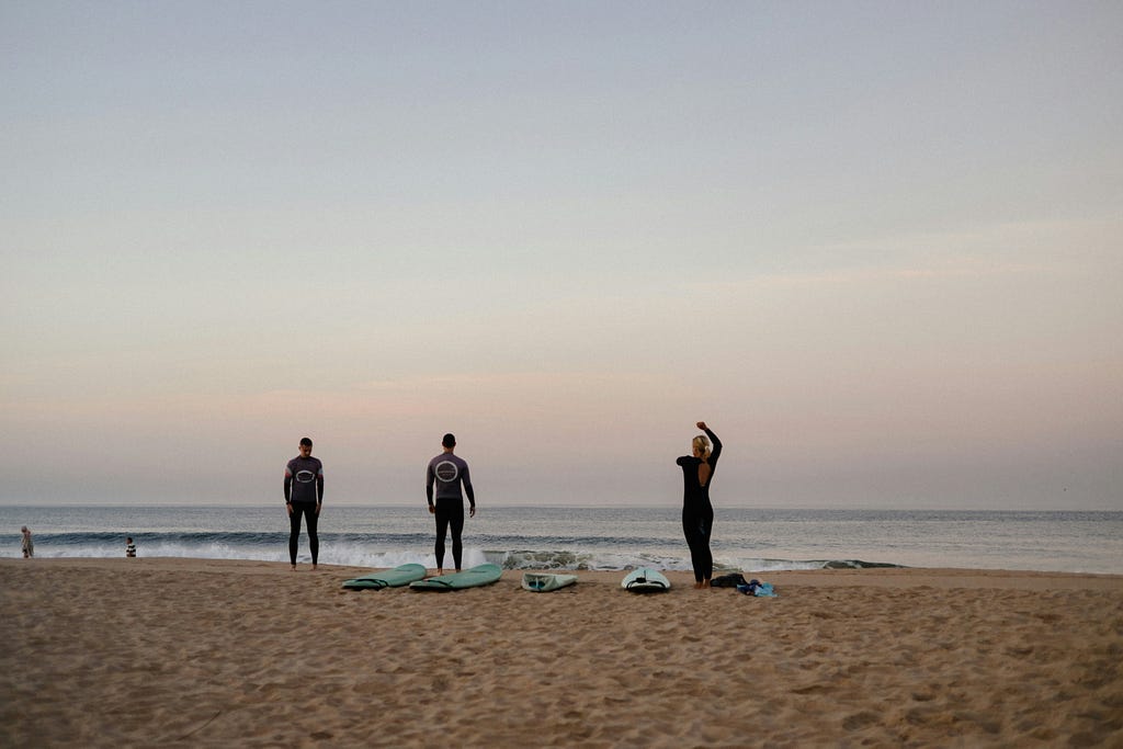 Three people at the beach preparing to surf.