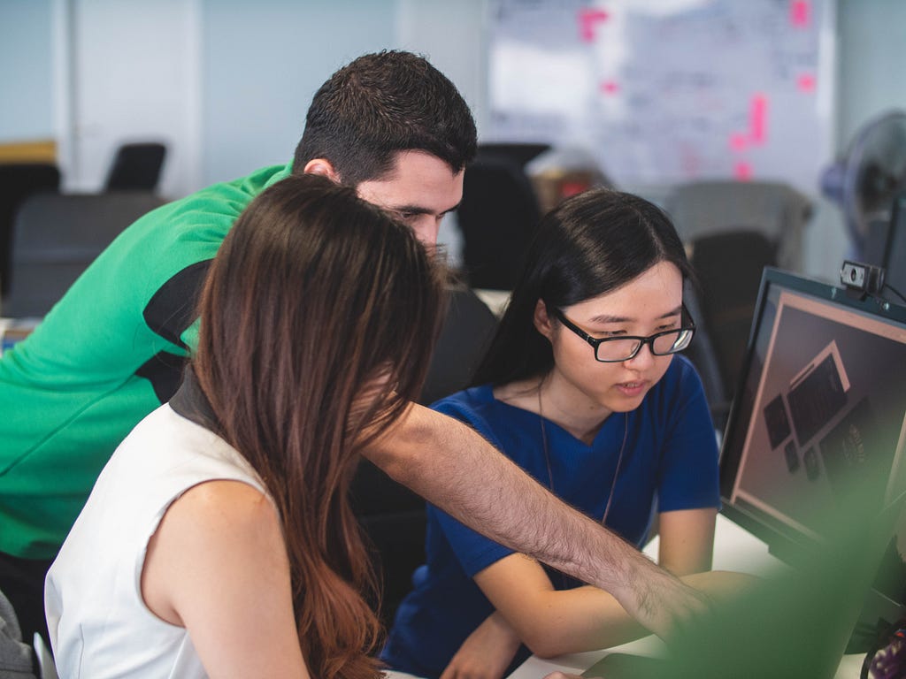 A group of 3 co-workings looking at a computer screen.