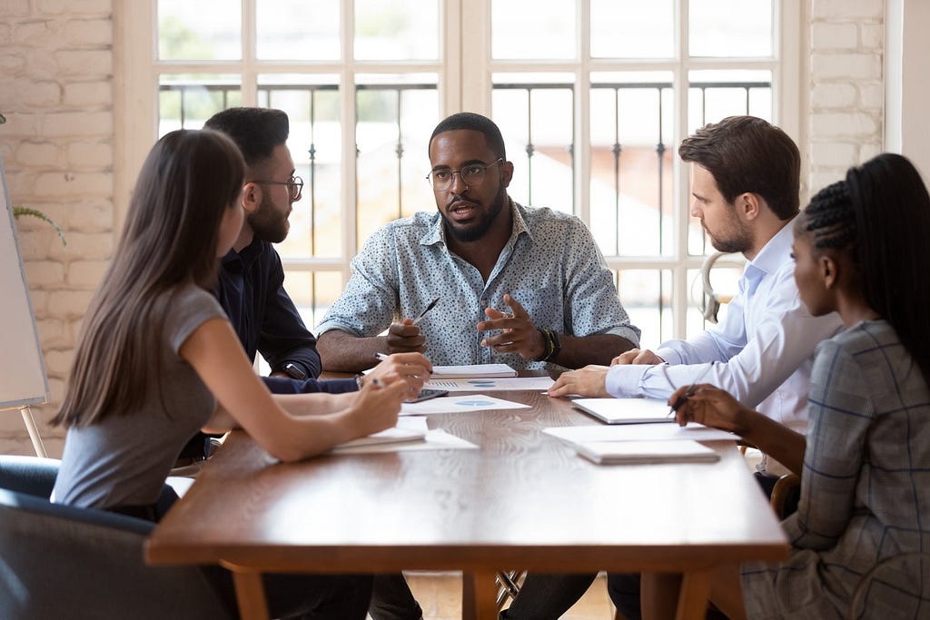 A project manager is having a conversation with his team. Projects often require diverse teams from every background with every skill set.