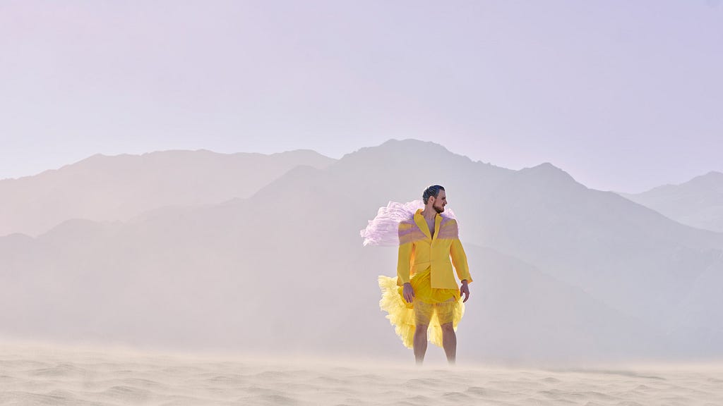 Young man in fashionable, yellow outfit standing in desert