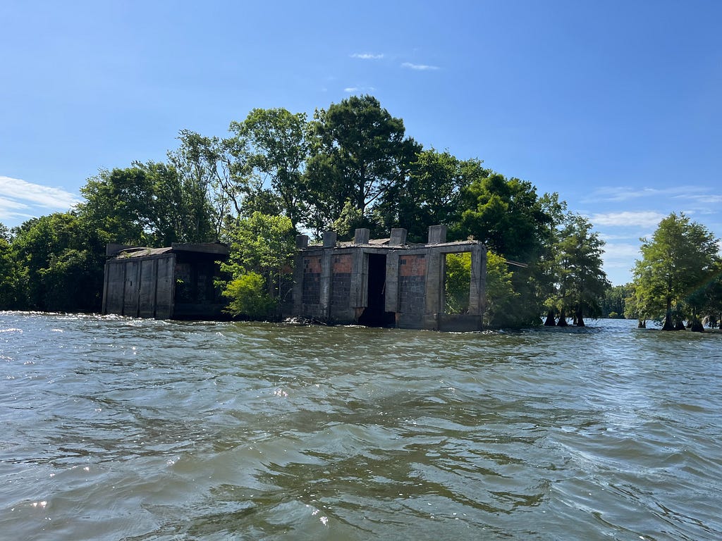 An image of the ruins of an old building, where you can see the concrete foundation. Trees surround it and the building is submerged in water.