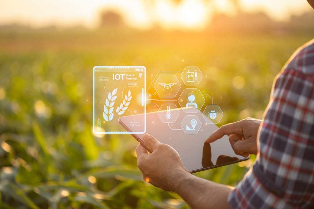 A farmer uses a tablet in front of a green crop on a farm. Numerous icons signifying data being collected and analyzed appear in an overlay that appear in front of the image.