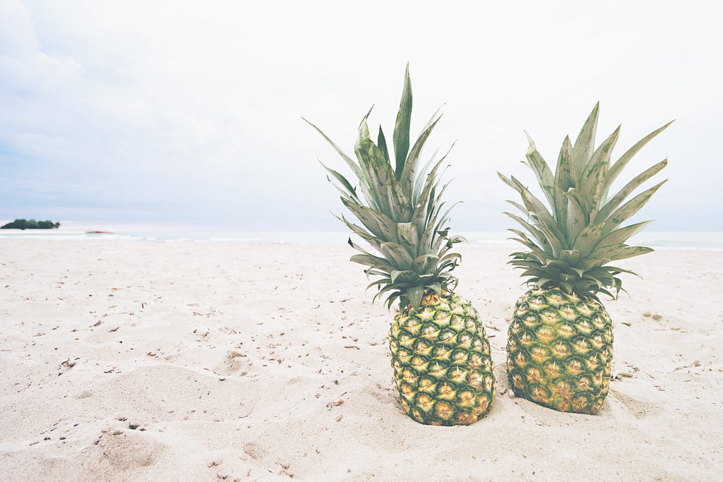 Two very similarly looking pineapples on the sand beach.