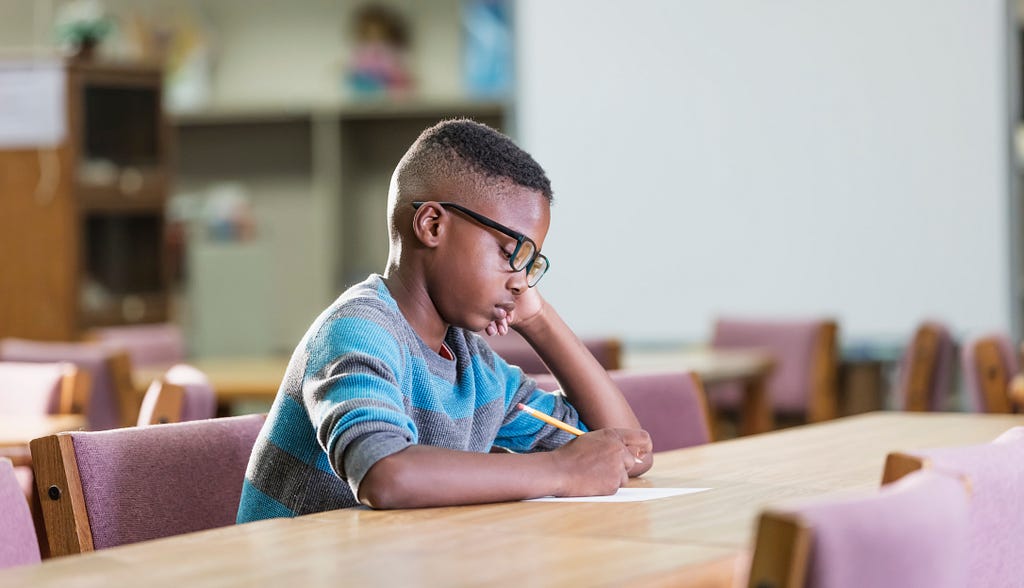 Young Black boy writes at a table. Photo by kali9/Getty Images