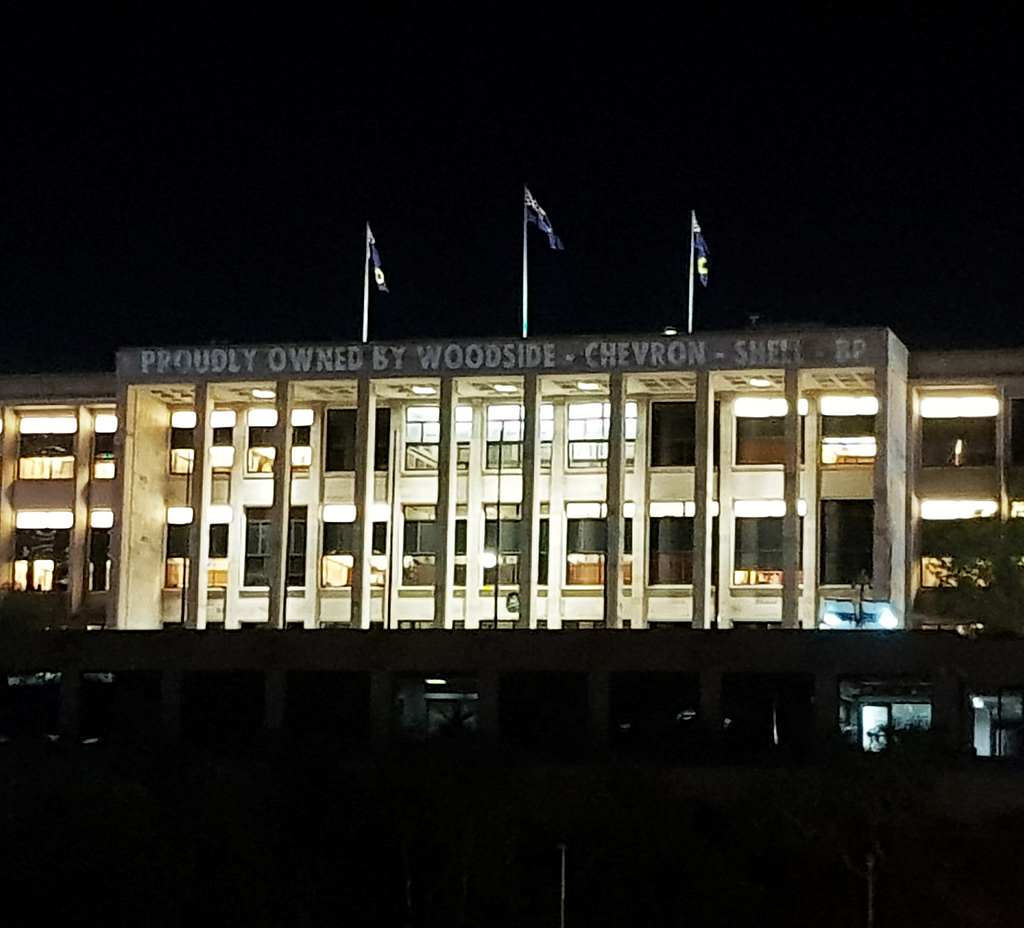 West Australia’s parliament house with the words “Proudly Owned by Woodside — Chevron — Shell — BP” projected directly onto it.