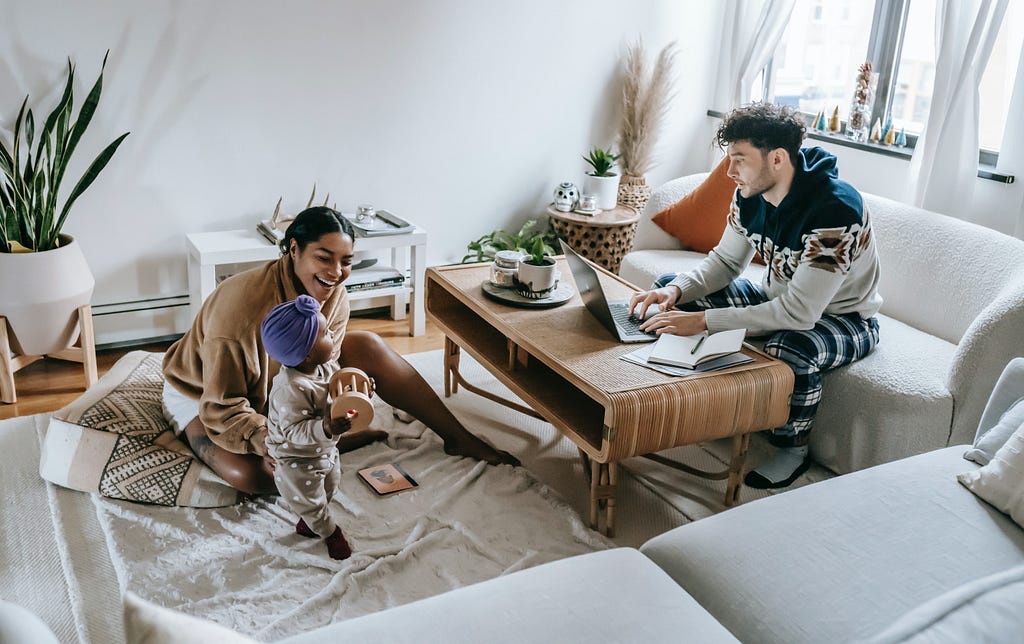 Working from home: A young couple play with their child in the living room, while one parent also works from a laptop