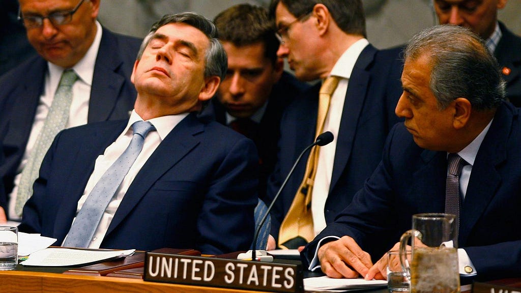 Diplomat sleeping at a meeting in front of four other people.