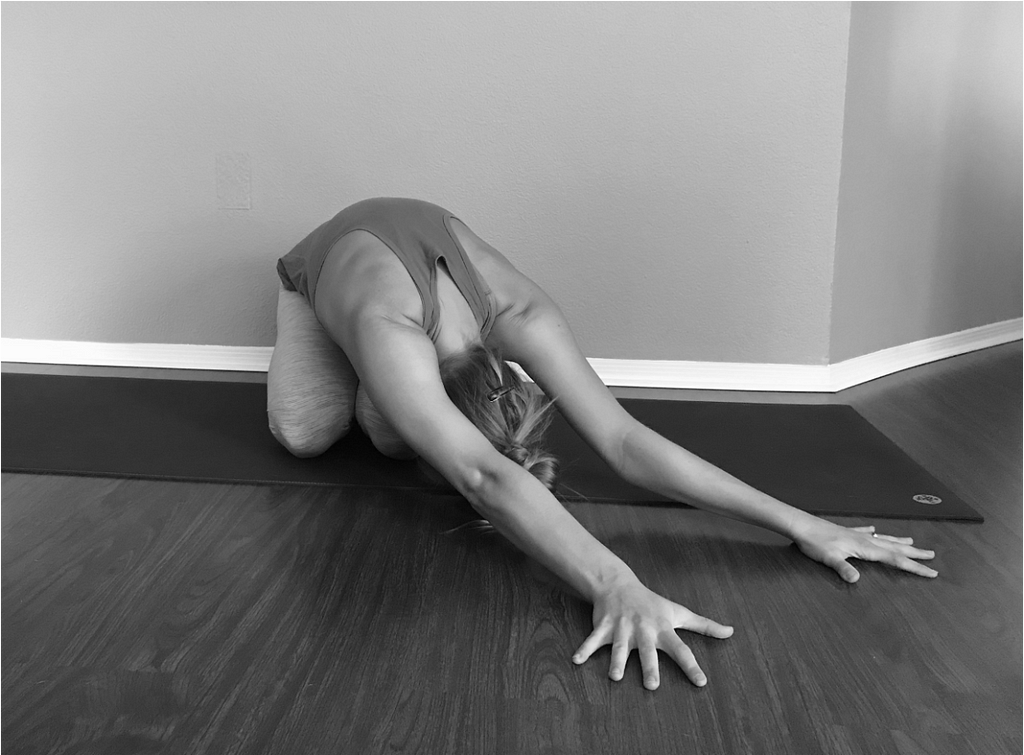 Black and white photo of a woman doing balasana, or child’s pose, on a yoga mat.