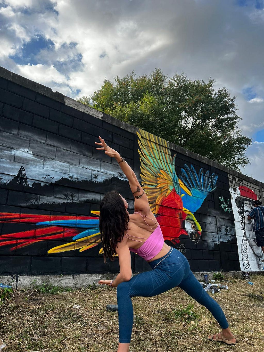Me in a yoga pose with all the arm jewelry, in front of a beautiful mural…a colorful bird in the foreground, black and white landscape in the back.