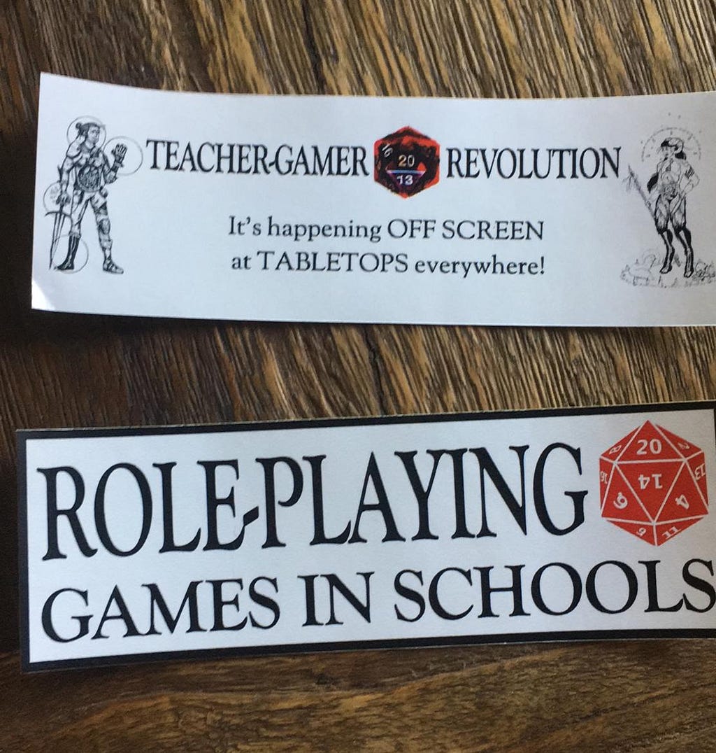 2 horizontal stickers 2x6 inch long on wood table. 1st says “Teacher-Gamer Revolution”, 2nd “Role-Playing Games in Schools”