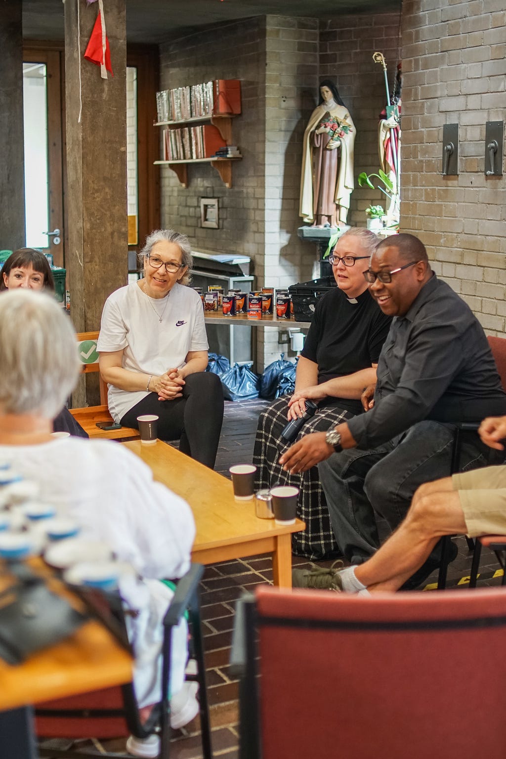 An image of six guests sitting around a table drinking coffee. The venue is a church and two obvious religious actors are part of the group.