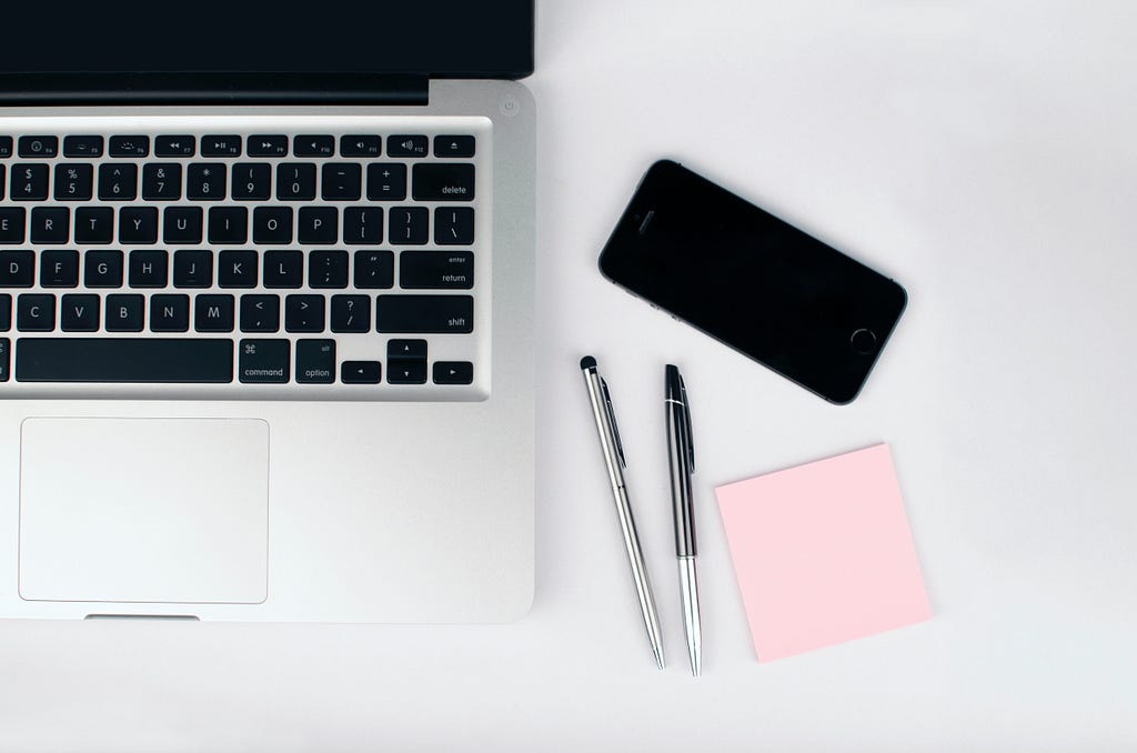 A picture of a laptop with a phone and some pens