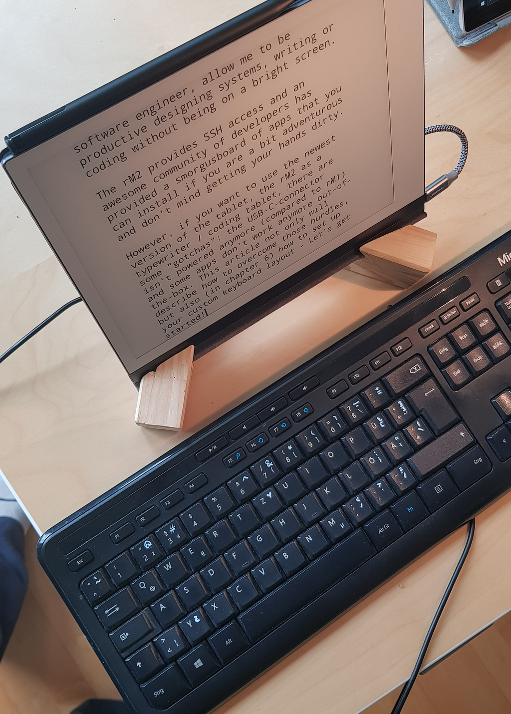 The reMarkable 2 tablet on a desk on a wooden stand. The keyboard is in front of it.