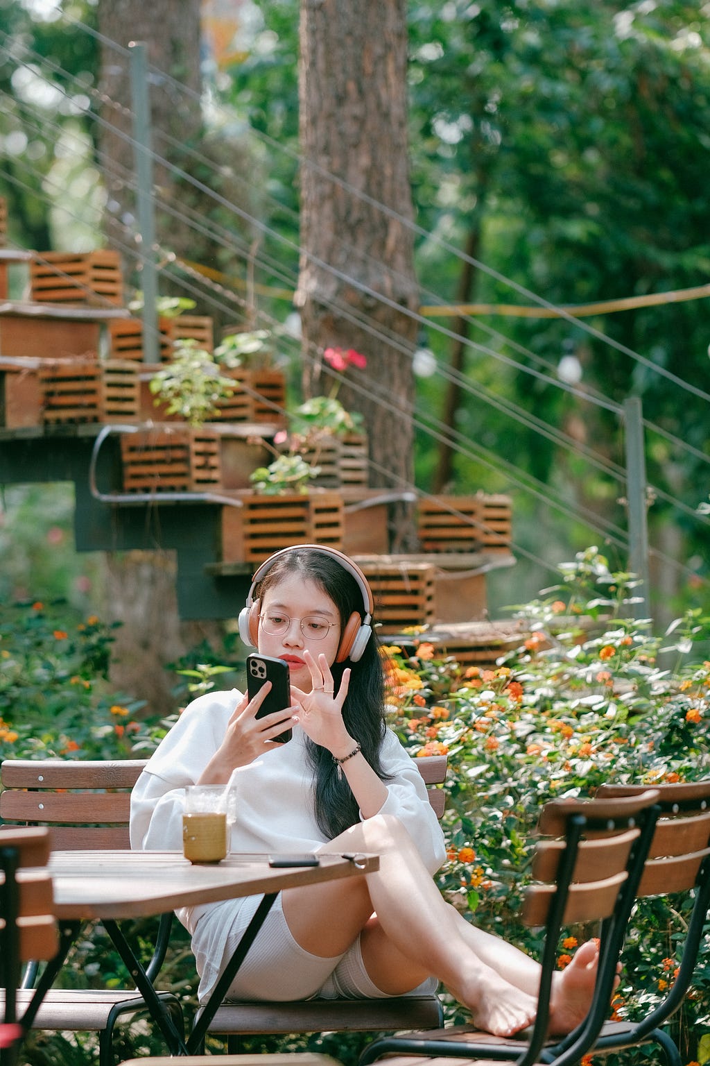 Young girl in headphones holding smartphone in her hands, sitting in picturesque cafe with coffee on the table