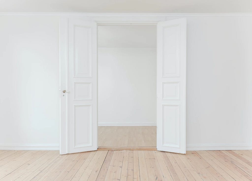 A white double-door on a white wall opening to a white room