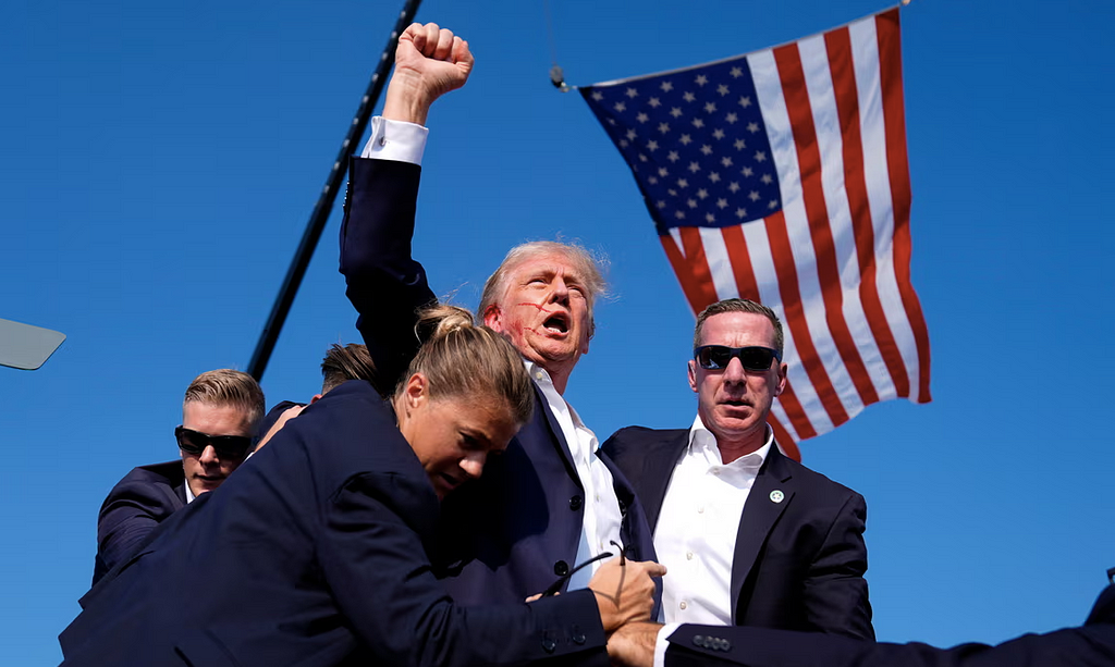 viral image of trump fist pumping the crown with blood on his face after assasination attempt surrounded by secret service and americna flag flying in background