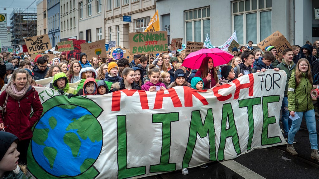A group of young people marching through a city street holding a sign that reads “March for Climate” with a picture of the earth.
