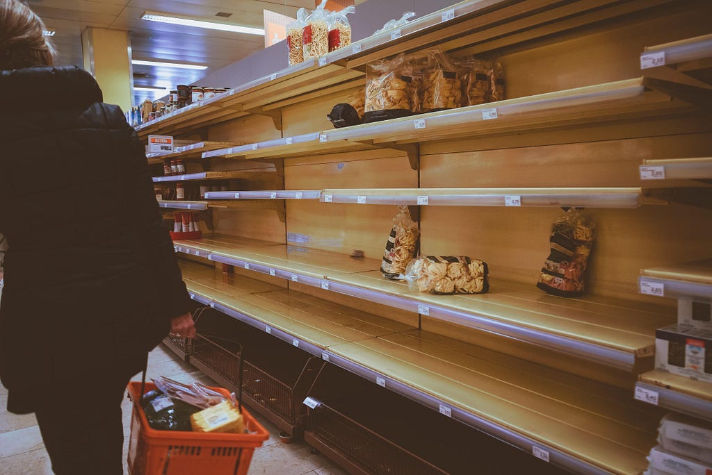 Photo of almost empty shelves due to Covid in a Swiss grocery store. A person is walking on the left with a red basket filled with items.