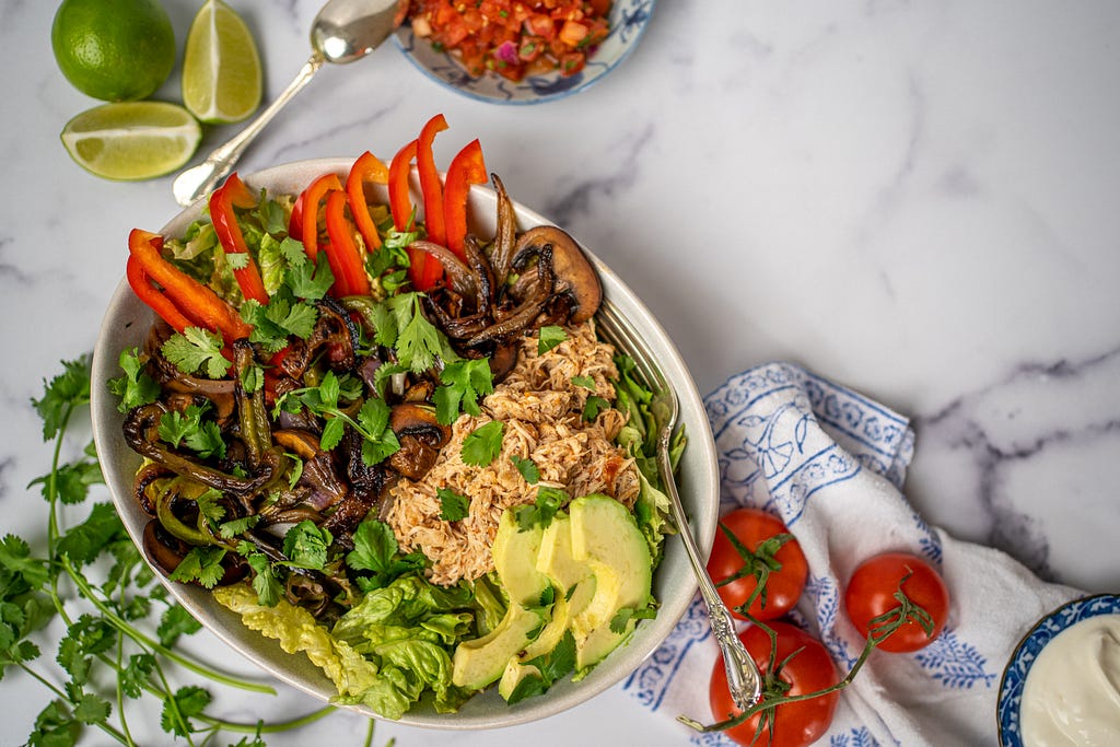 A large bowl filled with salad, chicken, fajita vegetables, and avocado.