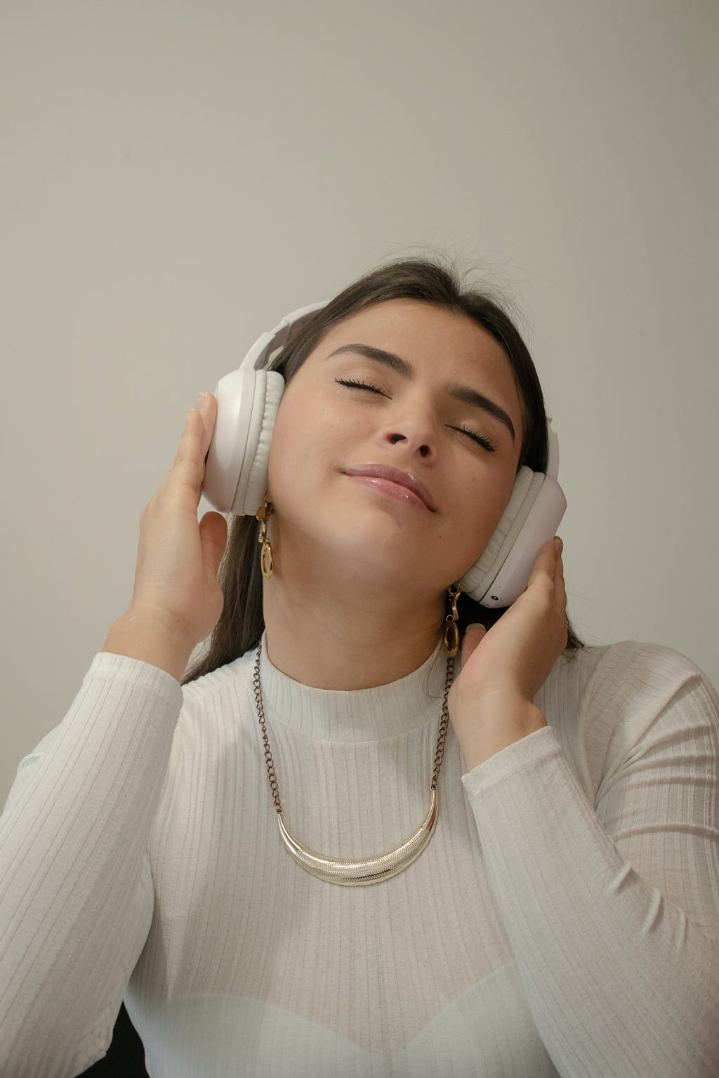 Money mindset: Girl in white and cream with eyes closed wearing overhead white headphones