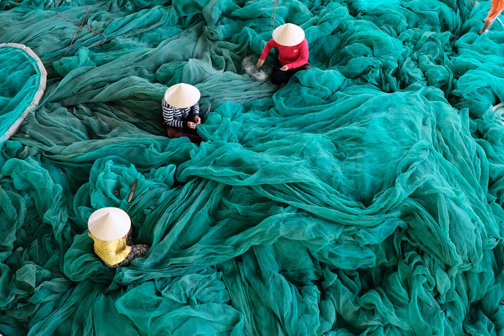 People working to repair and tend to vast fluffy piles of fine fish netting