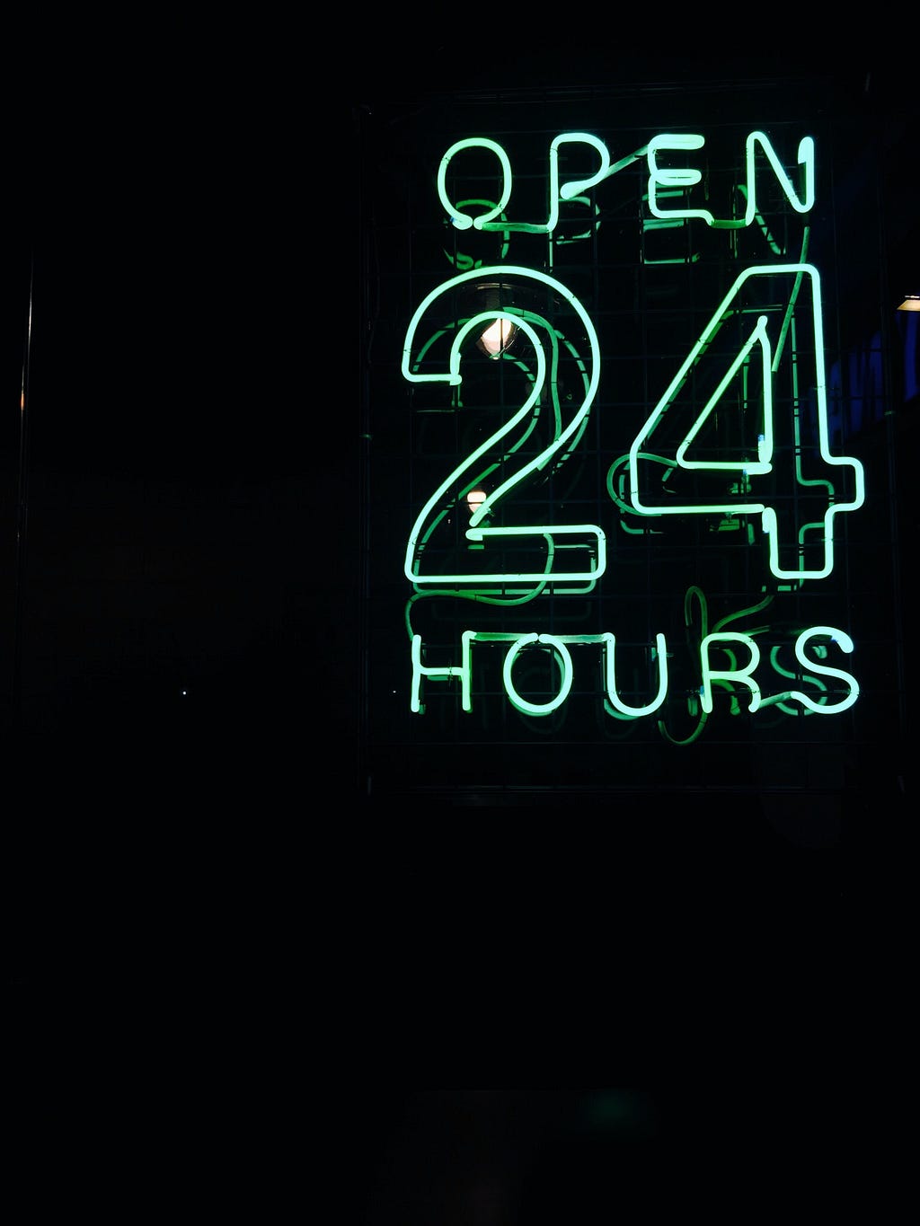 Placa em neon, com as palavras “Aberto 24 horas” brilhando em um azul claro