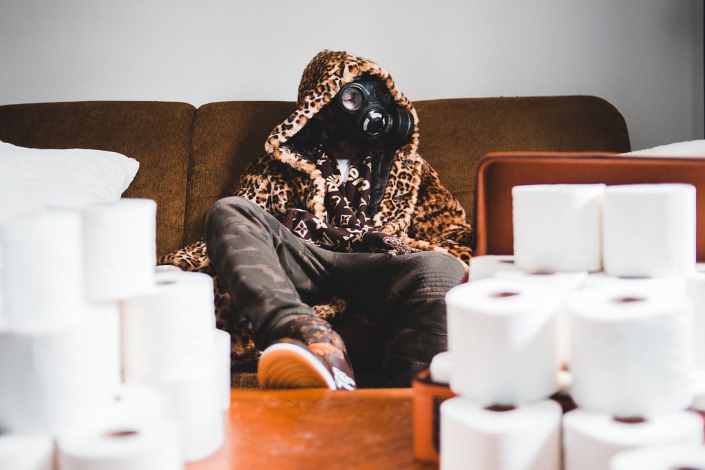 Man in a gas mask sit in front of a pile of toilet napkins rolls.