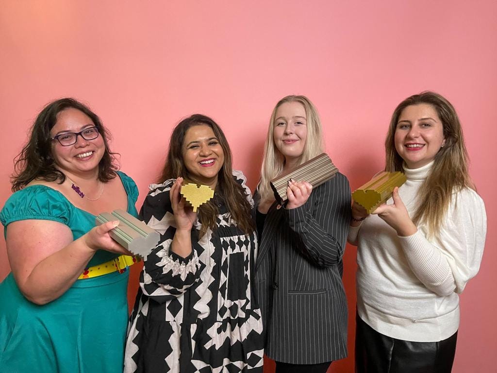 The Chayn team, from L to R, Sara, Hera, Emma and Dina, are standing and holding up the The Lovie Awards, trophies in the shape of a pixelated heart.