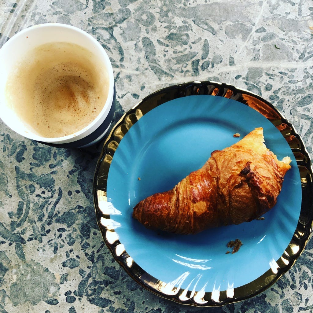 A croissant on a plate with one bite taken out of the end and a cup of coffee